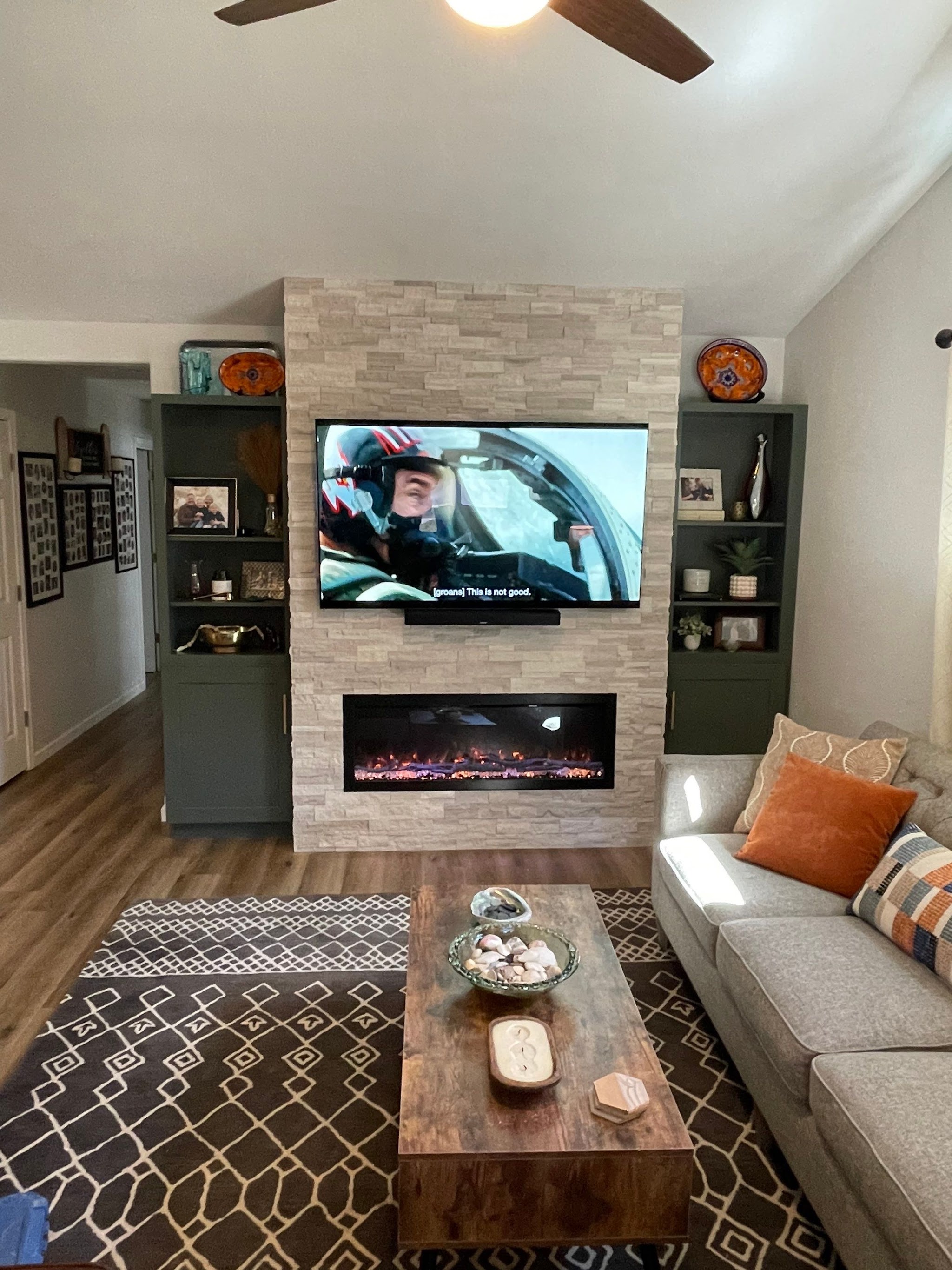 A finished living room with a stacked stone fireplace wall and built-in shelving