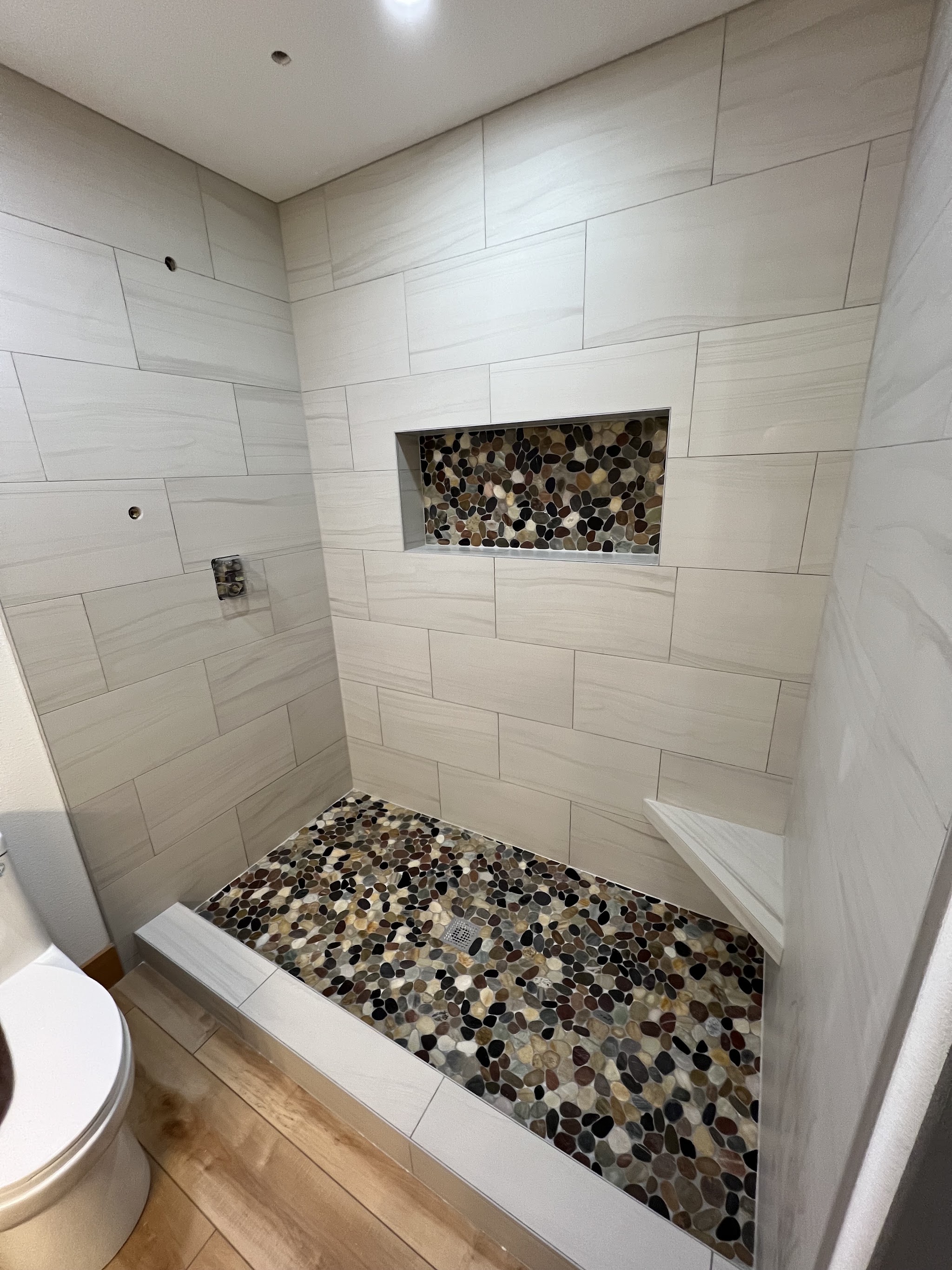 A finished shower with a pebble tile floor and built-in stone niche